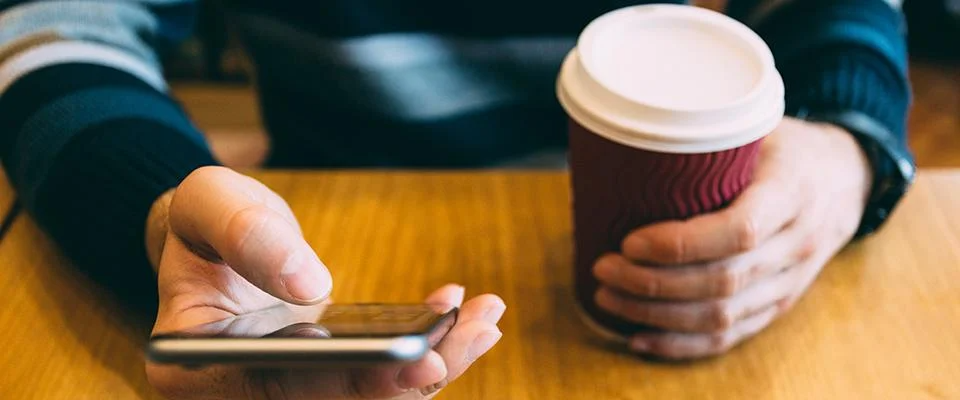 Mann bedient ein Smartphone mit einem Kaffe in der anderen Hand