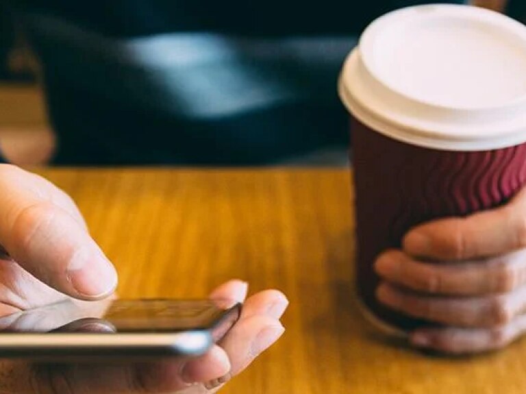 Mann bedient ein Smartphone mit einem Kaffe in der anderen Hand